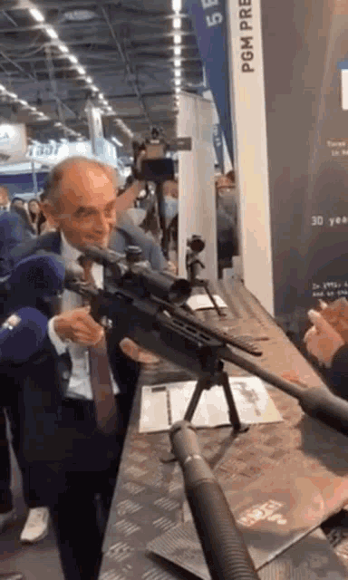a man in a suit and tie is standing in front of a sniper rifle with the word pom on it