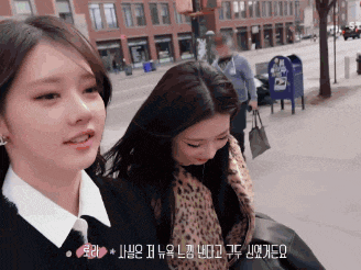 two girls are walking down a street with a blue mailbox behind them
