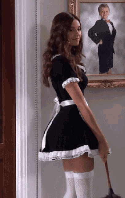 a woman in a maid costume is holding a mop in front of a painting of a man in a tuxedo