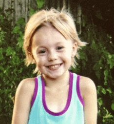 a young girl wearing a blue tank top with a purple trim smiles for the camera