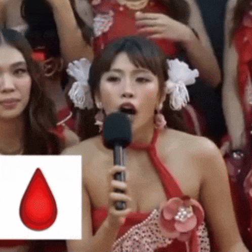 a woman in a red dress is holding a microphone in front of a picture of a blood drop