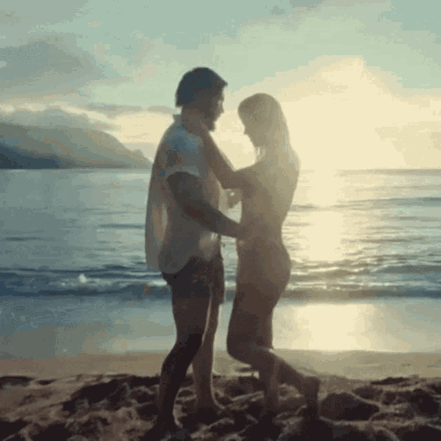 a man and a woman are dancing on a beach at sunset .