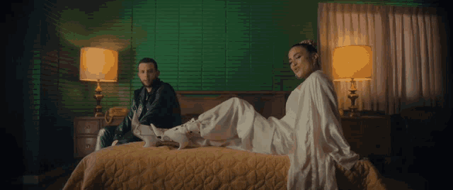 a man sits on a bed next to a woman who is laying on a bed