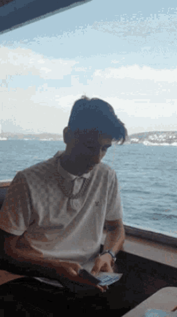 a man in a louis vuitton shirt is sitting in front of a window overlooking a body of water