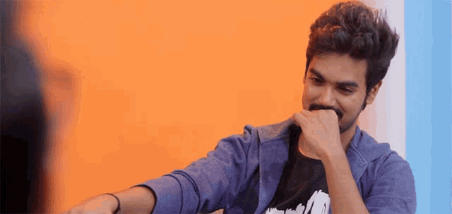 a man covering his mouth with his hand while wearing a purple jacket and a black shirt