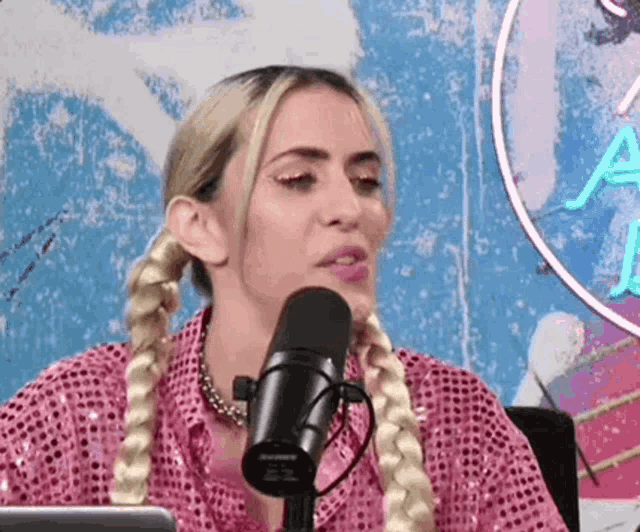a woman is sitting in front of a microphone wearing a pink shirt and braids .