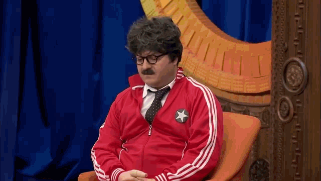 a man wearing glasses and a red jacket is sitting in a chair .