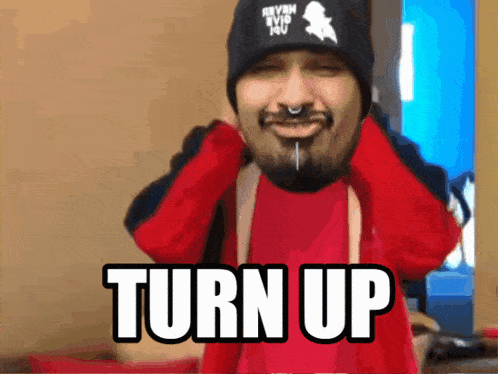 a man with a beard is wearing a red shirt and a black hat that says turn up on it