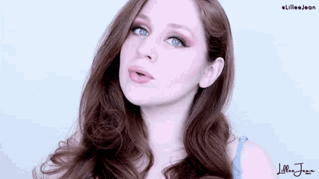 a woman with long red hair and blue eyes is wearing a blue tank top