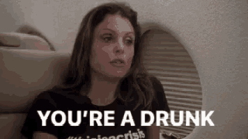 a woman is sitting on a plane with the words `` you 're a drunk '' written on her shirt .