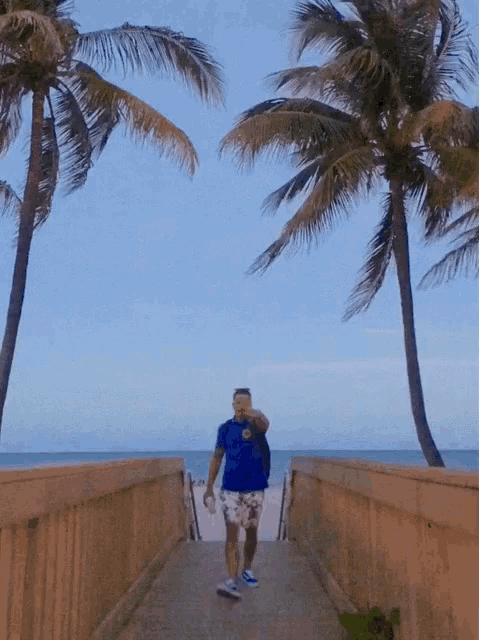 a man in a blue shirt takes a picture of himself while walking towards the beach