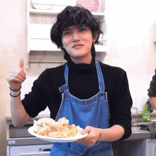 a person wearing an apron holds a plate of food and gives a thumbs up