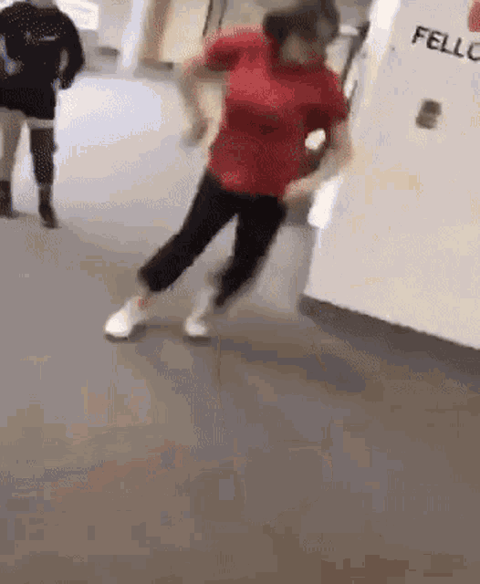 a woman in a red shirt and black pants is dancing on the floor in a hallway .