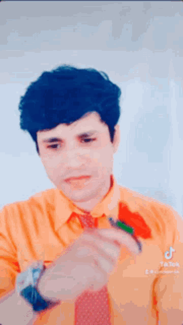 a man in an orange shirt and red tie is holding a red rose in his hand