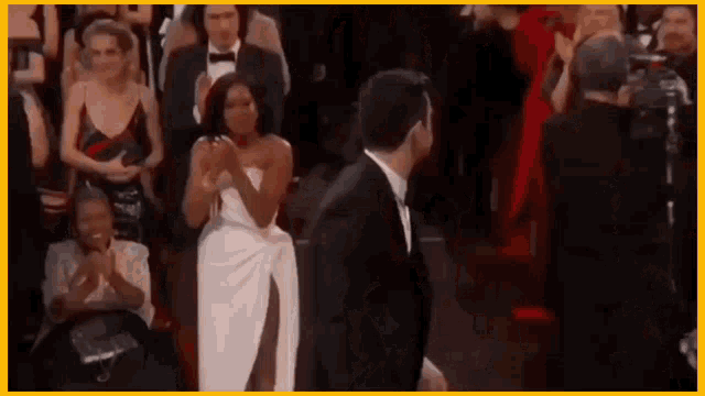 a man in a tuxedo and a woman in a white dress are standing next to each other in front of a crowd .