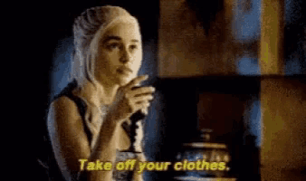 a woman is standing in a dark room holding a glass of wine and saying `` take off your clothes '' .