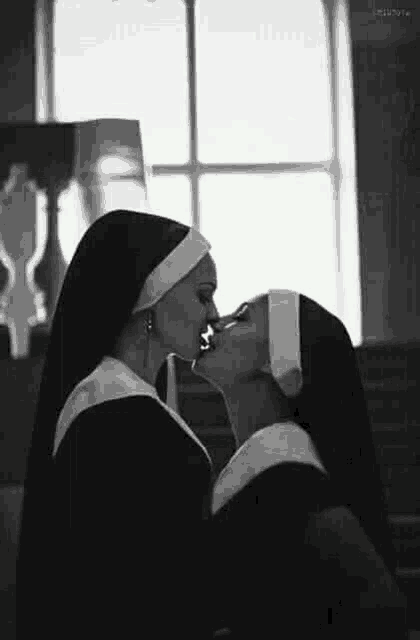 a black and white photo of two nuns kissing each other in a church .