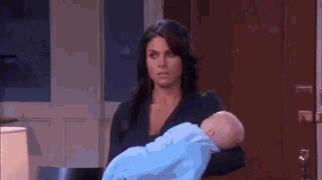 a woman is holding a baby in her arms and looking at it .