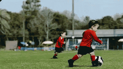 a boy in a red shirt kicking a soccer ball on a field