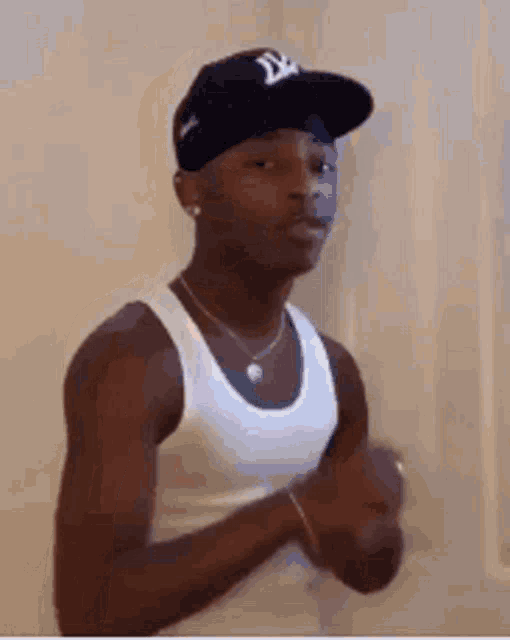 a young man wearing a hat and a white tank top is standing in a room .