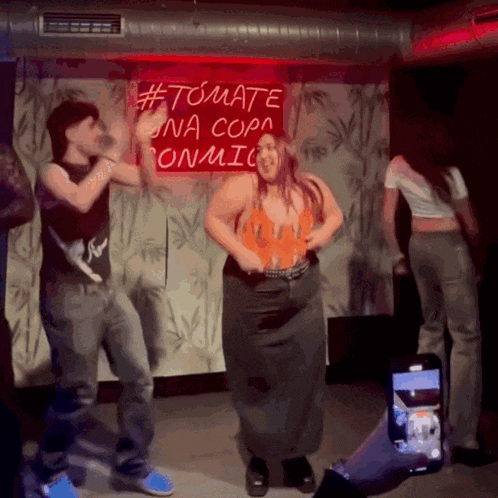 a woman is dancing in front of a neon sign that says #tomate na copa onmic