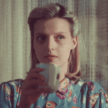 a woman in a blue floral shirt is holding a cup of coffee