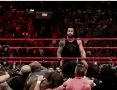a wrestler is jumping in the air in a wrestling ring while a crowd watches .