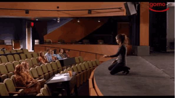 a woman is kneeling down in front of a microphone in a room with other women .
