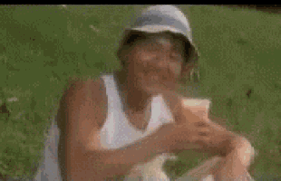 a man in a hat is sitting in the grass holding a cup of orange juice .