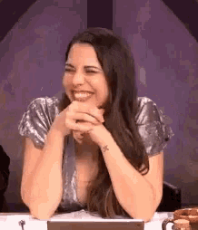 a woman is sitting at a table laughing with her hands folded .