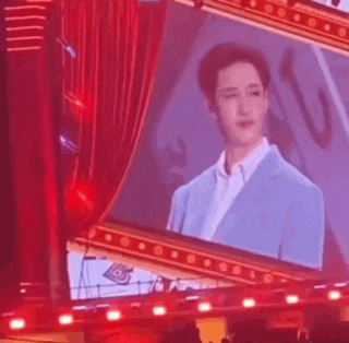 a man in a blue suit is standing in front of a red curtain on a stage holding a microphone .