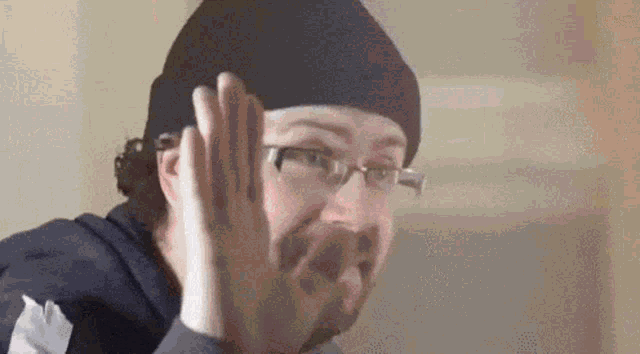 a man wearing glasses and a beanie is making a face .