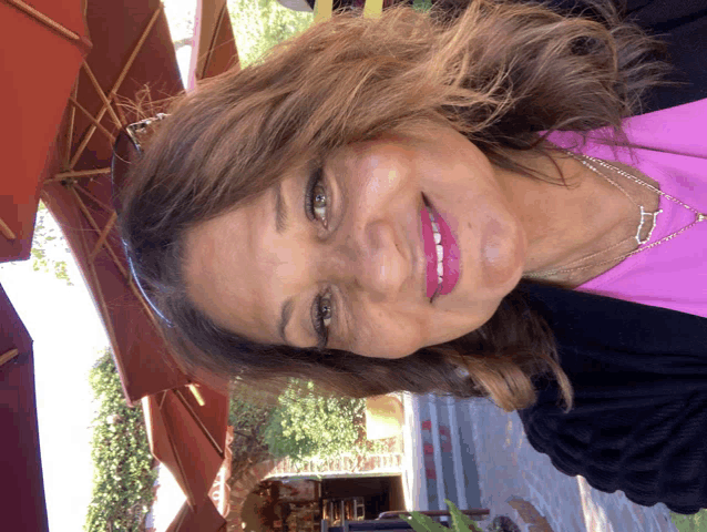 a woman in a pink shirt and black jacket smiles in front of a red umbrella