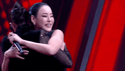 a woman is hugging another woman while holding a microphone .
