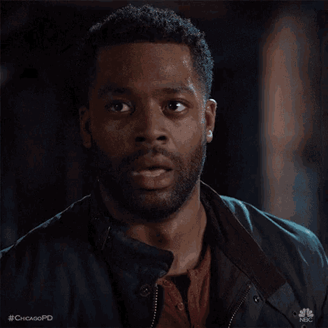 a man with a beard is wearing a jacket and a red shirt and making a surprised face .
