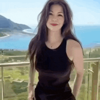 a woman in a black tank top is standing on a balcony overlooking a body of water .