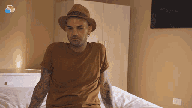 a man wearing a hat sits on a bed in front of a tv
