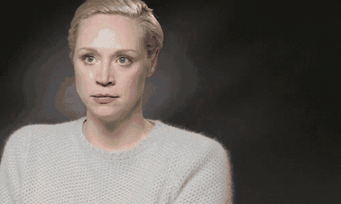 a woman wearing a grey sweater is making a funny face and looking at the camera .