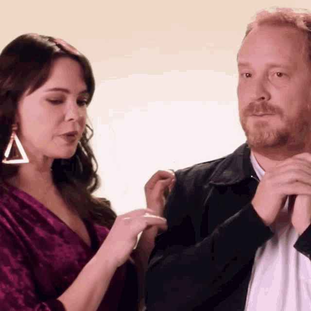 a man and a woman are standing next to each other and the woman is wearing a triangle earring