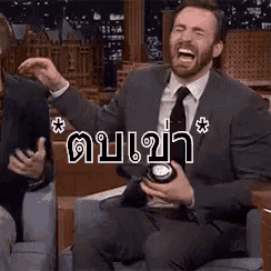 a man in a suit and tie is sitting on a couch laughing .
