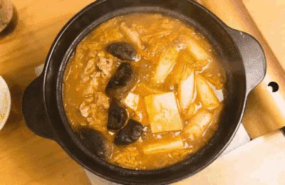 a pot of soup with meat and vegetables is being cooked on a stove top .