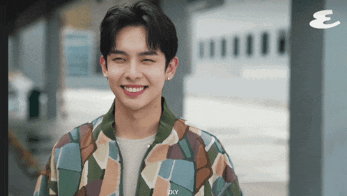 a young man in a camouflage jacket is smiling with the letter e in the background