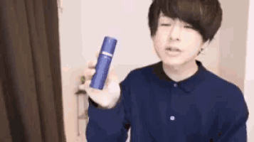 a young man in a blue shirt is holding a blue bottle of something .