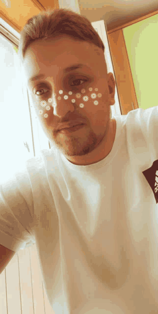 a man with flowers painted on his face is wearing a white adidas t-shirt