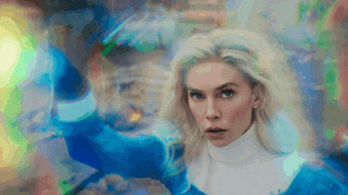 a woman in a blue sweater and white turtleneck stands in front of a colorful background