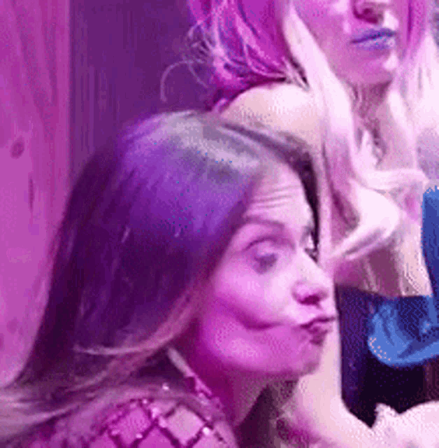 a woman with purple hair is making a funny face in front of a purple light .