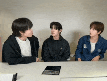 three young men are sitting at a table with a tablet in front of them and one of them has a jacket with the number 33 on it