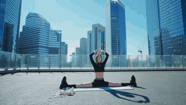 a woman is doing a split on a mat in front of tall buildings