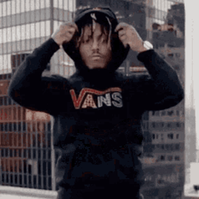 a man wearing a black vans hoodie is standing in front of a tall building .