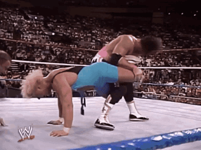 two wrestlers are fighting in a wrestling ring with a crowd watching .